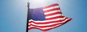 United States Flag on the Blue Sky Illuminated by Sun. Large USA Flag on the High Metal Pole.